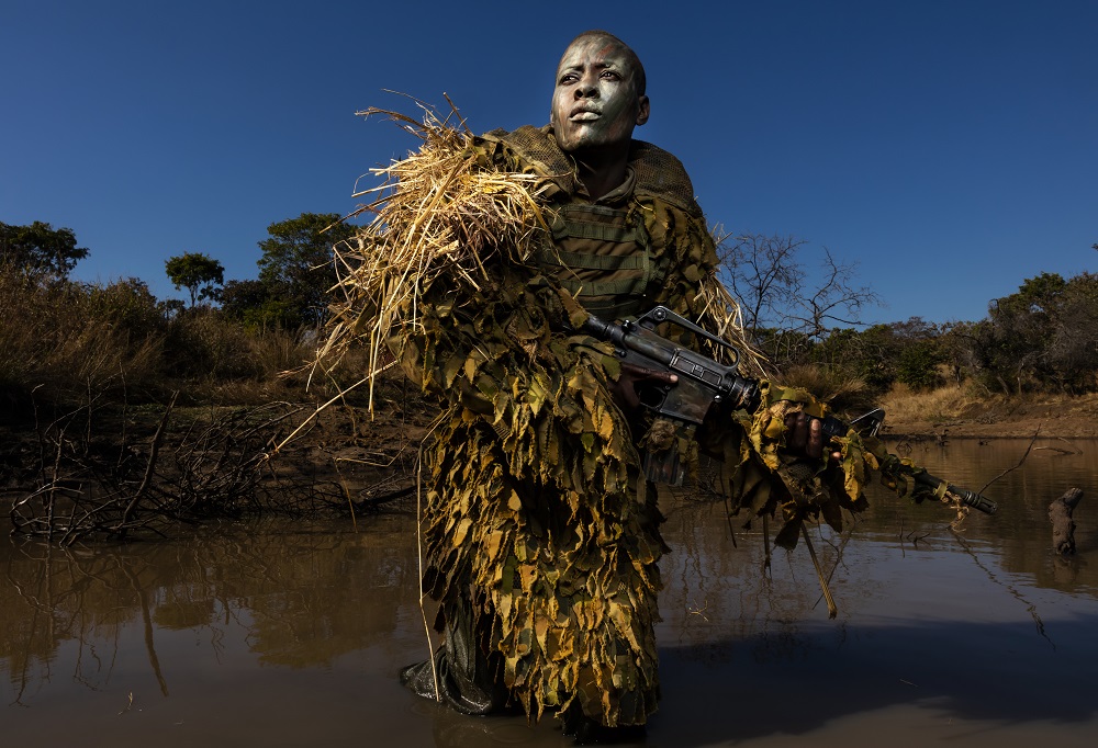 PHUNDUNDU WILDLIFE AREA, ZIMBABWE, JUNE 2018: Petronella Chigumbura, 30, an elite member of the all female conservation ranger force known as Akashinga undergoes sniper movement and concealment training in the bush near their base. Akashinga (meaning the ‘Brave Ones’ in local dialect) is a community-driven conservation model, empowering disadvantaged women to restore and manage a network of wilderness areas as an alternative to trophy hunting. Many current western-conceived solutions to conserve wilderness areas struggle to gain traction across the African continent. Predominately male forces are hampered by ongoing corruption, nepotism, drunkenness, aggressiveness towards local communities and a sense of entitlement. The I.A.P.F, the International Anti-Poaching Foundation led by former Australian Special Forces soldier Damien Mander, was created as a direct action conservation organisation to be used as a surgical instrument in targeting wildlife crime. In 2017 they decided to innovate, using an all- female team to manage an entire nature reserve in Zimbabwe. The program builds an alternative approach to the militarized paradigm of ‘fortress conservation’ which defends colonial boundaries between nature and humans. While still trained to deal with any situation they may face, the team has a community-driven interpersonal focus, working with rather than against the local population for the long-term benefits of their own communities and nature.