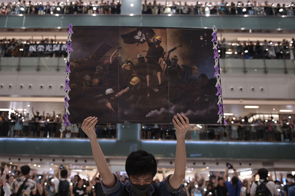 A man holds a poster as others gather at a shopping mall in the Shatin area of Hong Kong on September 11, 2019, to sing a recently penned protest song titled 'Glory to Hong Kongí which has been gaining popularity in the city. (Photo by Nicolas ASFOURI / AFP)