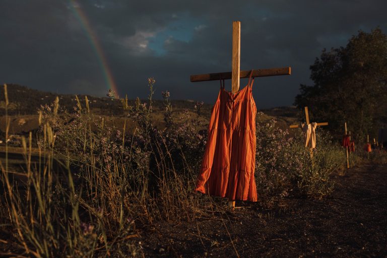 Dress hanging on cross behin which is a field, a rainbow and a dark sky